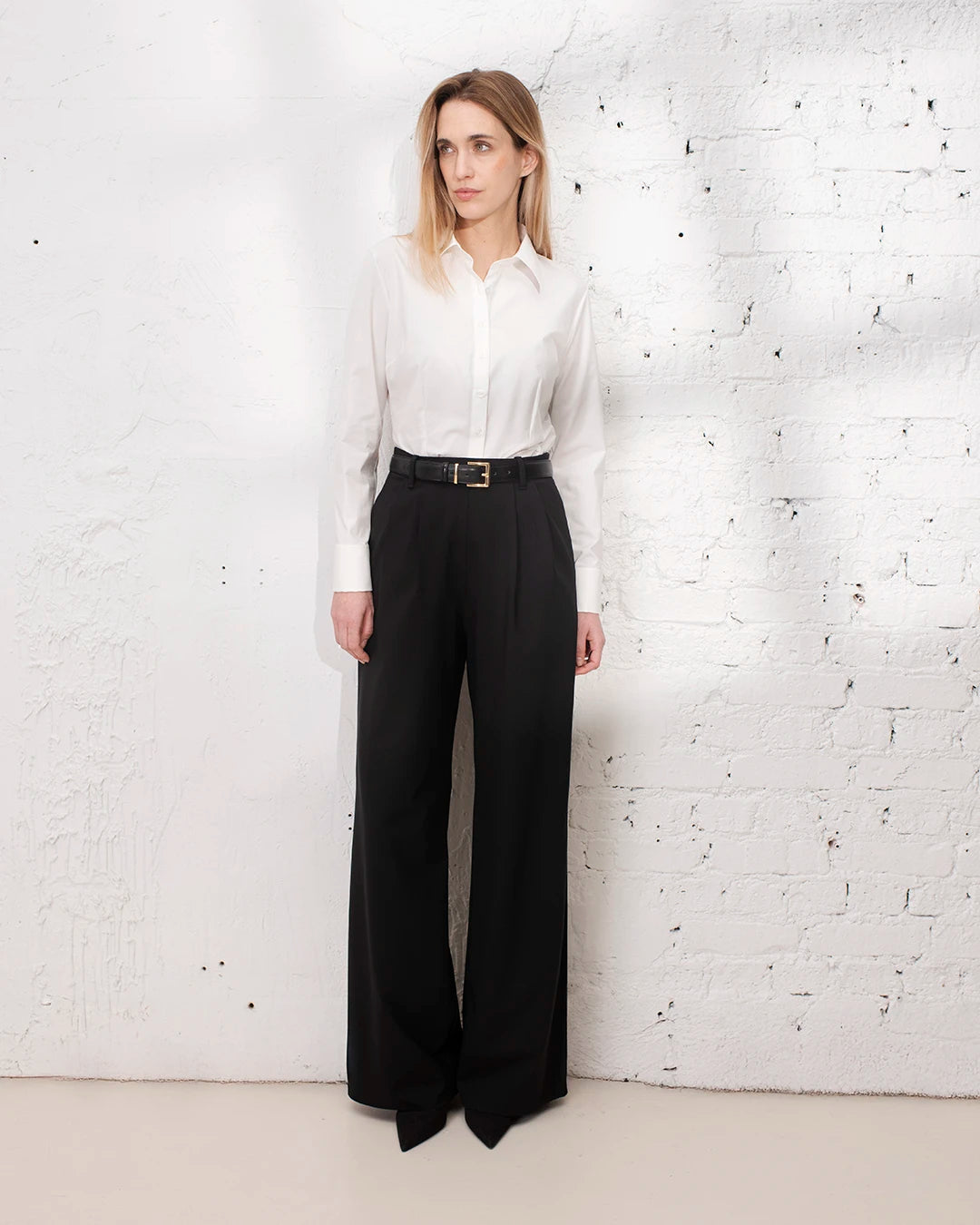 Tenue de bureau femme avec chemise blanche cintrée et pantalon tailleur large noir.